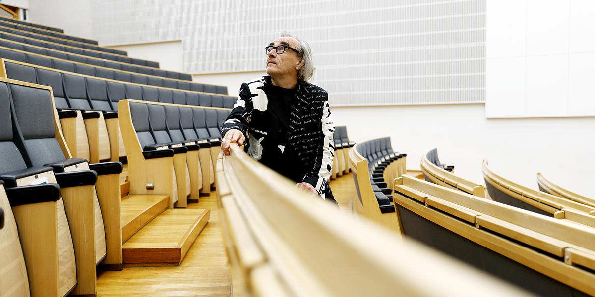 Filosofi Esa Saarinen istuu luentosalin penkillä penkin selkänojaan nojaten ja katsoo ylöspäin.