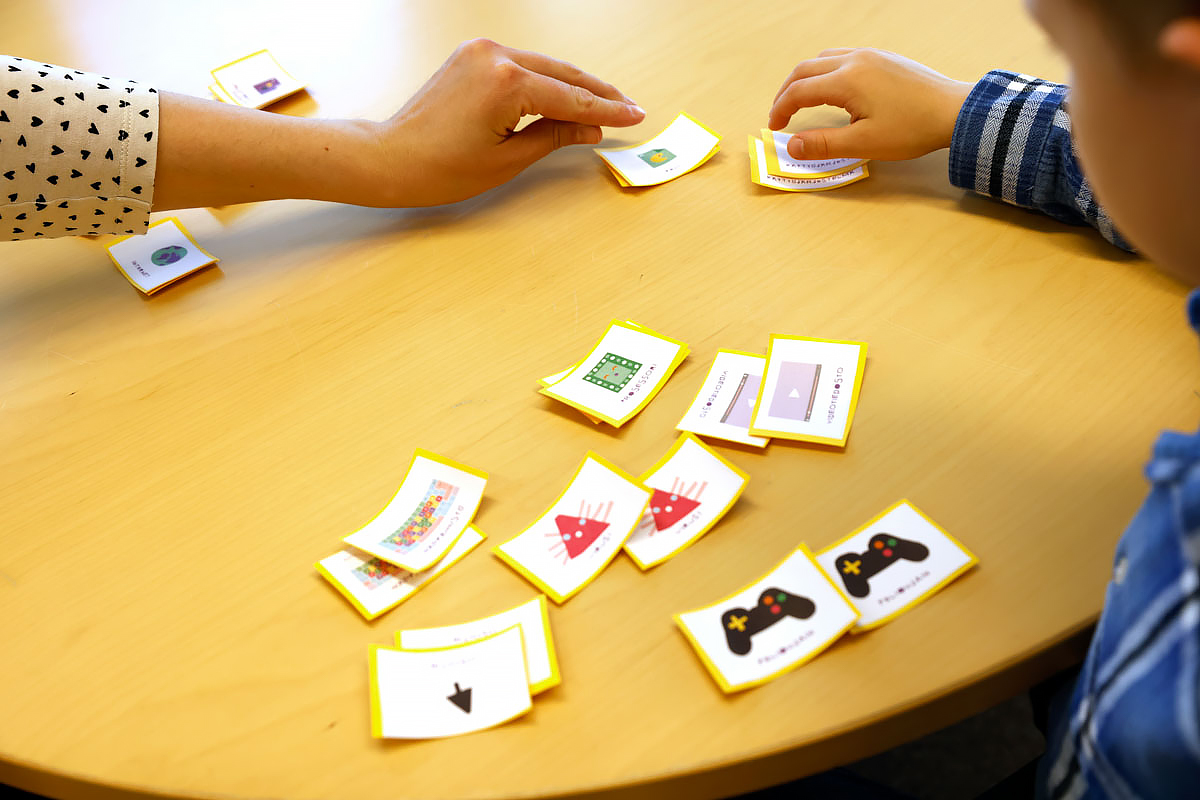 Pöydälle on levitetty kortteja muistipelistä. Kaksi kättä tarttuu kortteihin kuvan oikealla ja vasemmalla puolella.