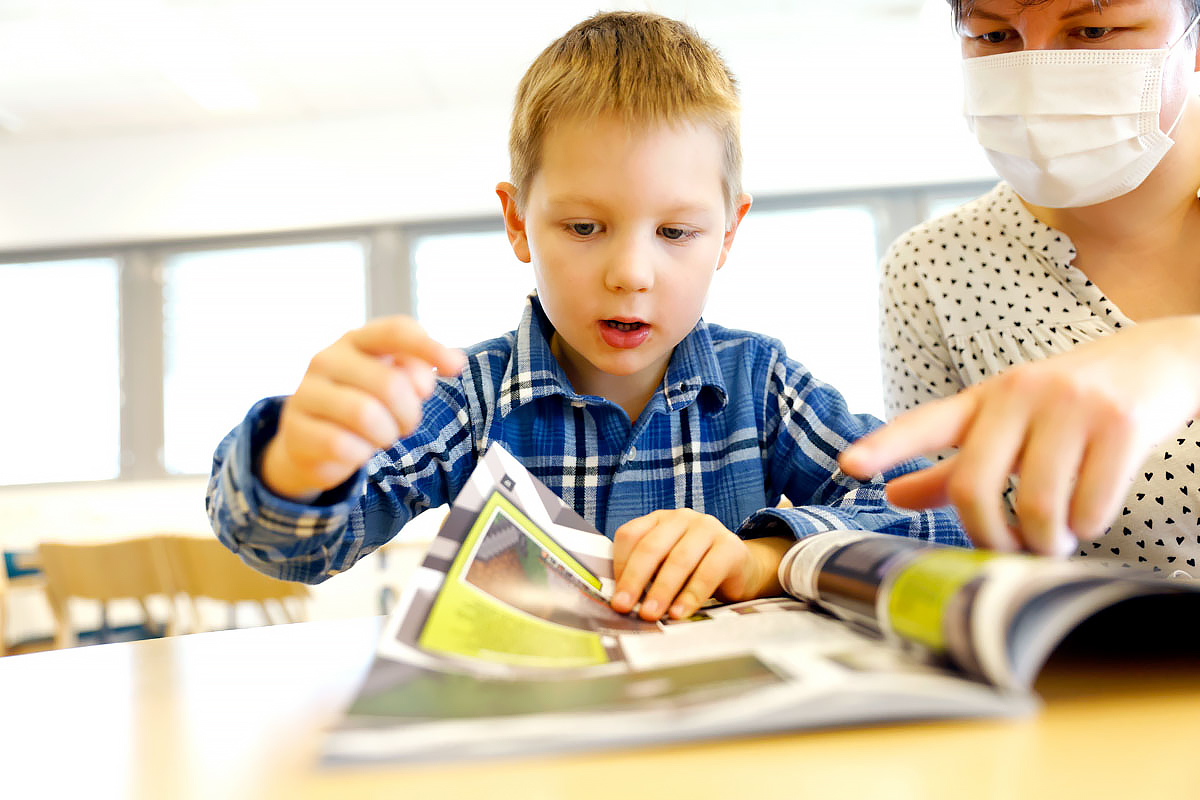 Lapsi ja aikuinen selaavat yhdessä pöydällä olevaa lehteä. 