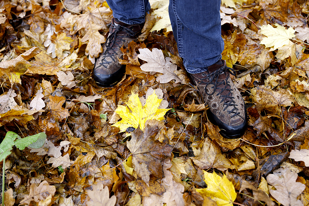 Valokuvassa haastateltava Esko Tainion jalat ja kengät kuvattuna vasten syksyisten lehtien peittämää maata.