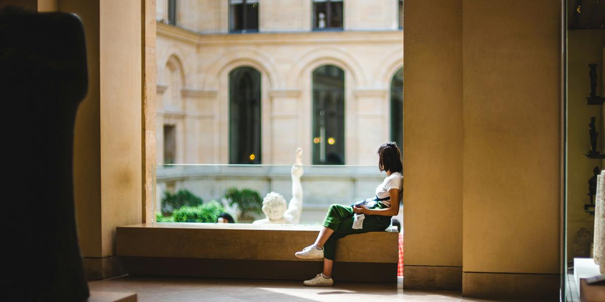 Henkilö istuu ikkunan syvennyksessä ajatuksiinsa uppoutuneena.