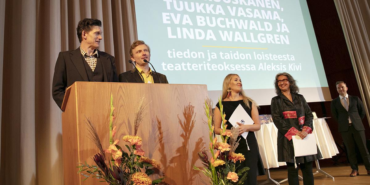 Kuvassa neljän hengen Aleksis Kivi -työryhmä ottaa vastaan vuoden 2022 tiedonjulkistamisen valtionpalkinnon Ravintola Töölön juhlasalin lavalla.