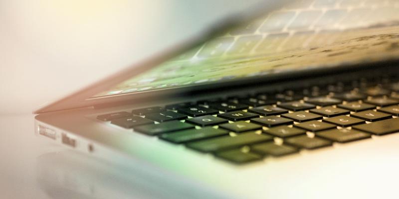 The image shows a grey laptop against a greyish background with hints of green and yellow.