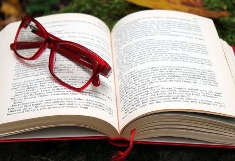 En uppslagen bok på mossa och höstlöv, glasögon med röda bågar på boken.